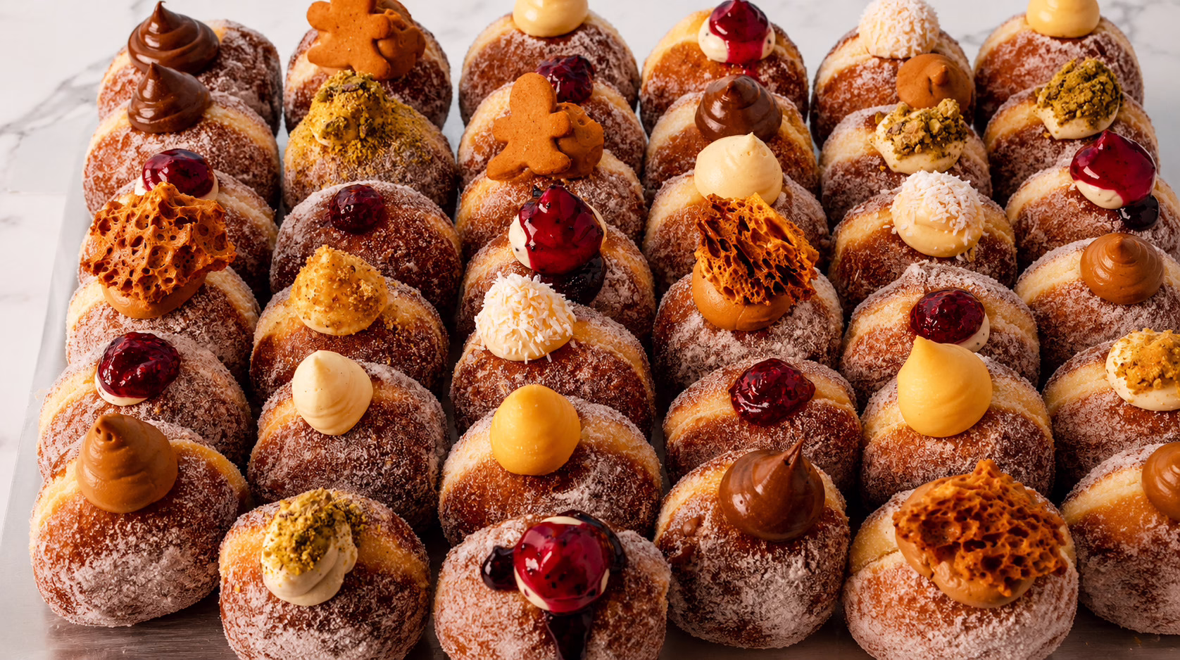 An assortment of Bread Ahead’s sugar-coated filled doughnuts topped with custards, chocolate, fruit compote and nut garnishes.