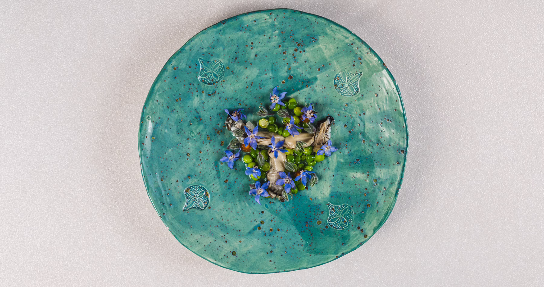 Peas, mushrooms and edible flowers served on a turquoise plate at Contraste in Milan