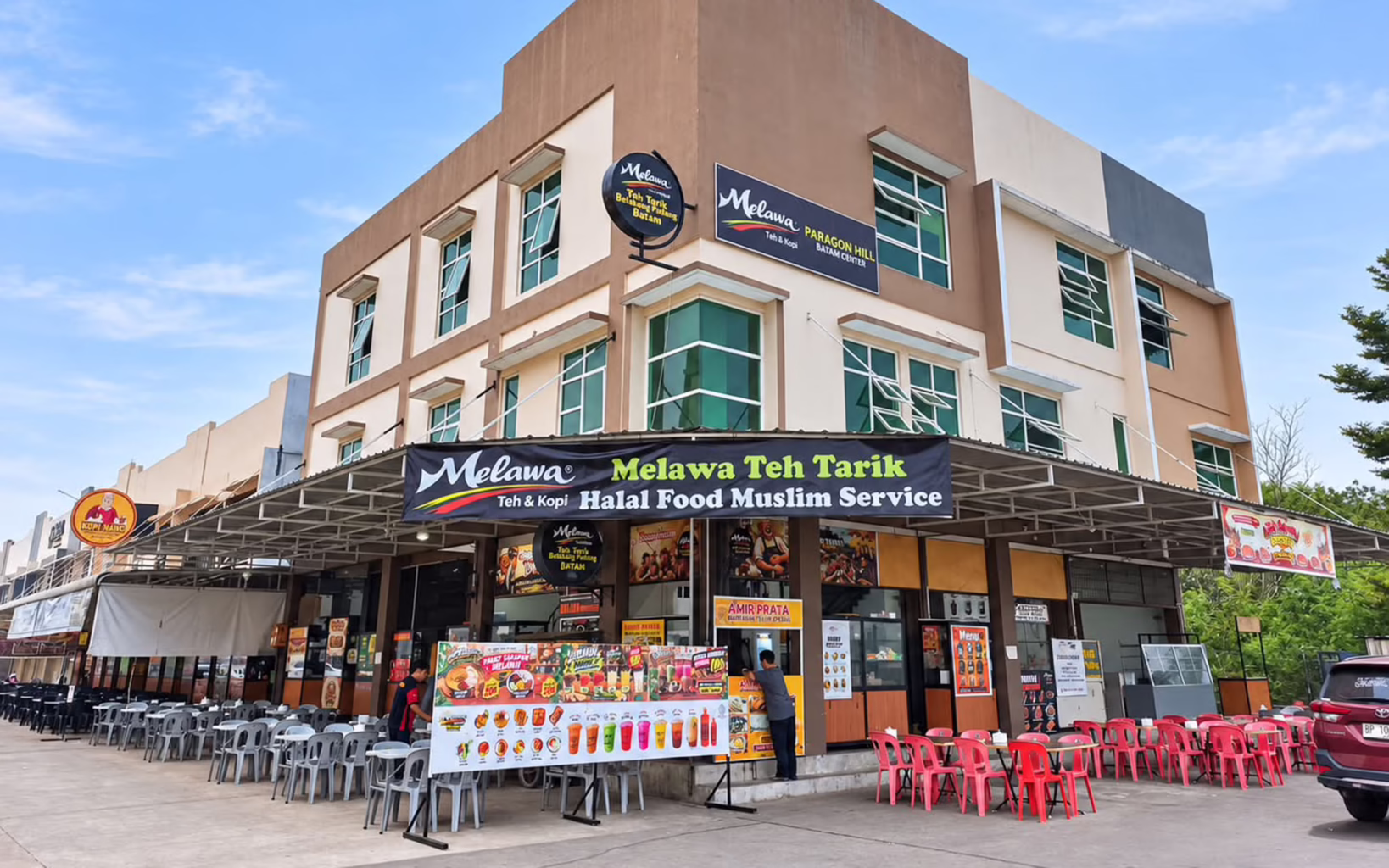 Exterior of Melawa Paragon Hill in Batam, featuring a three-storey building with restaurant signage, outdoor dining tables and colourful menu displays.