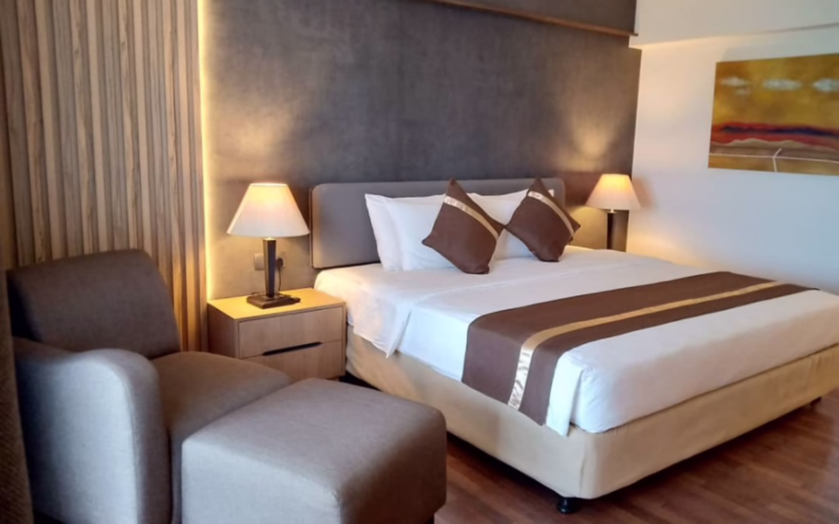 Guest bedroom at Sidjih Wellness Village in Batam, featuring a double bed, upholstered armchair, warm lighting and contemporary furnishings.