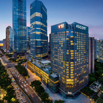 Aerial view of an Ascott serviced residence in Guangzhou at dusk, surrounded by illuminated skyscrapers, busy roads and the city's modern skyline.
