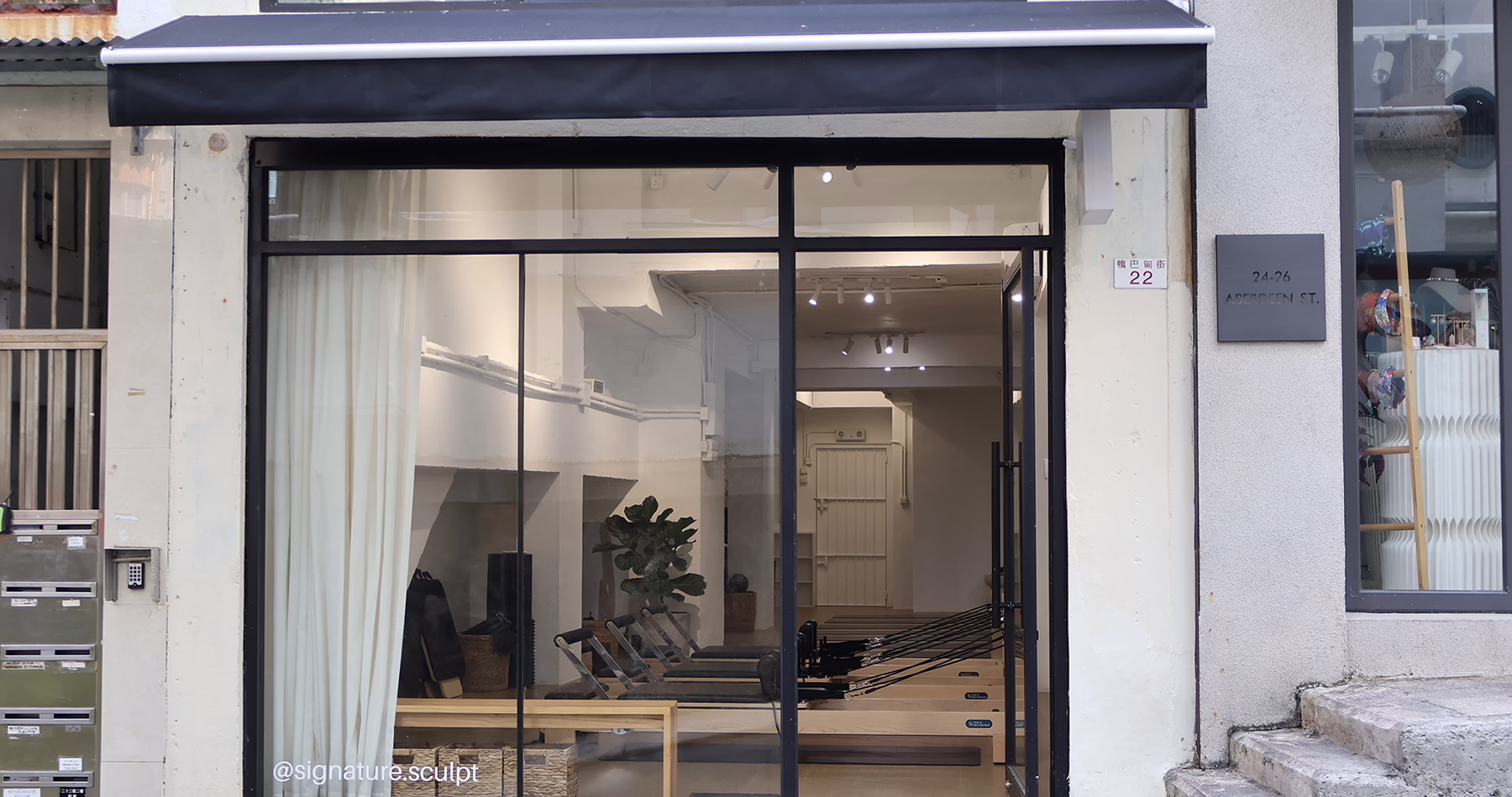 Street-level exterior of Signature Sculpt Pilates studio on Aberdeen Street in Hong Kong, featuring a glass-fronted entrance with wooden reformer machines visible inside.