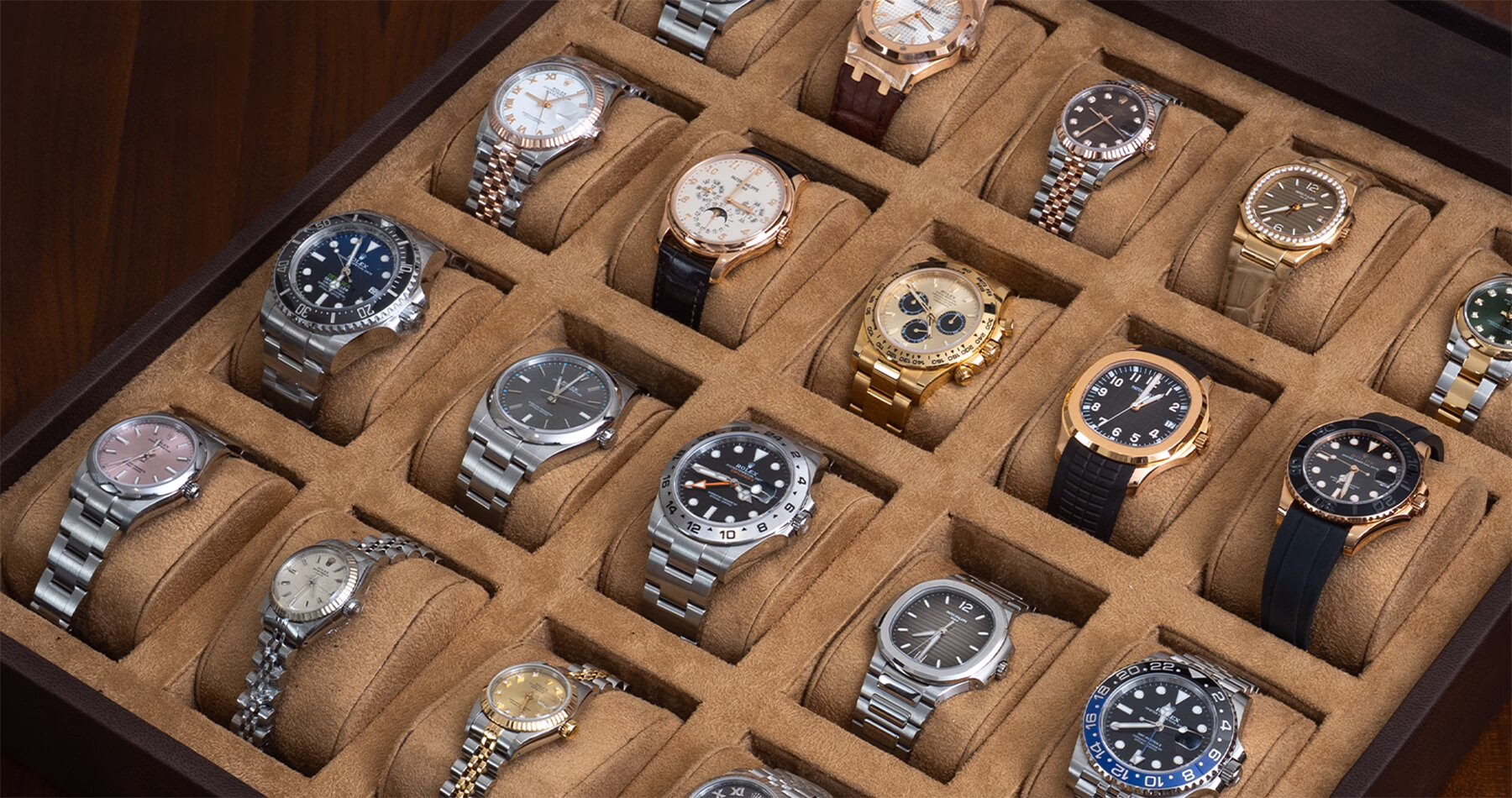 A collection of luxury wristwatches in stainless steel, gold and two-tone finishes, neatly arranged in a suede-lined display case.