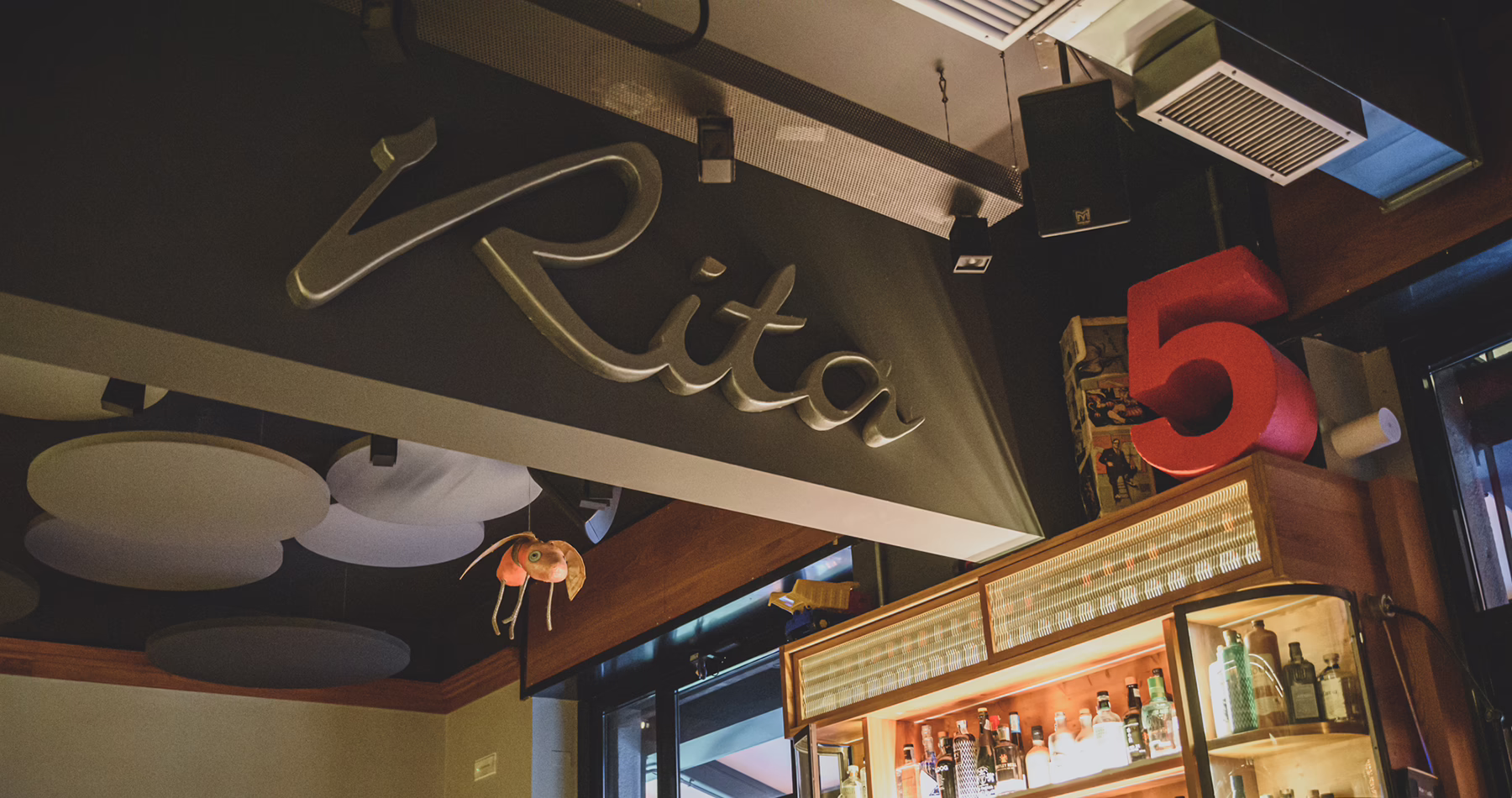 Rita cocktail bar in Milan, featuring its signature signage, illuminated spirits display and a large red number five above the bar.