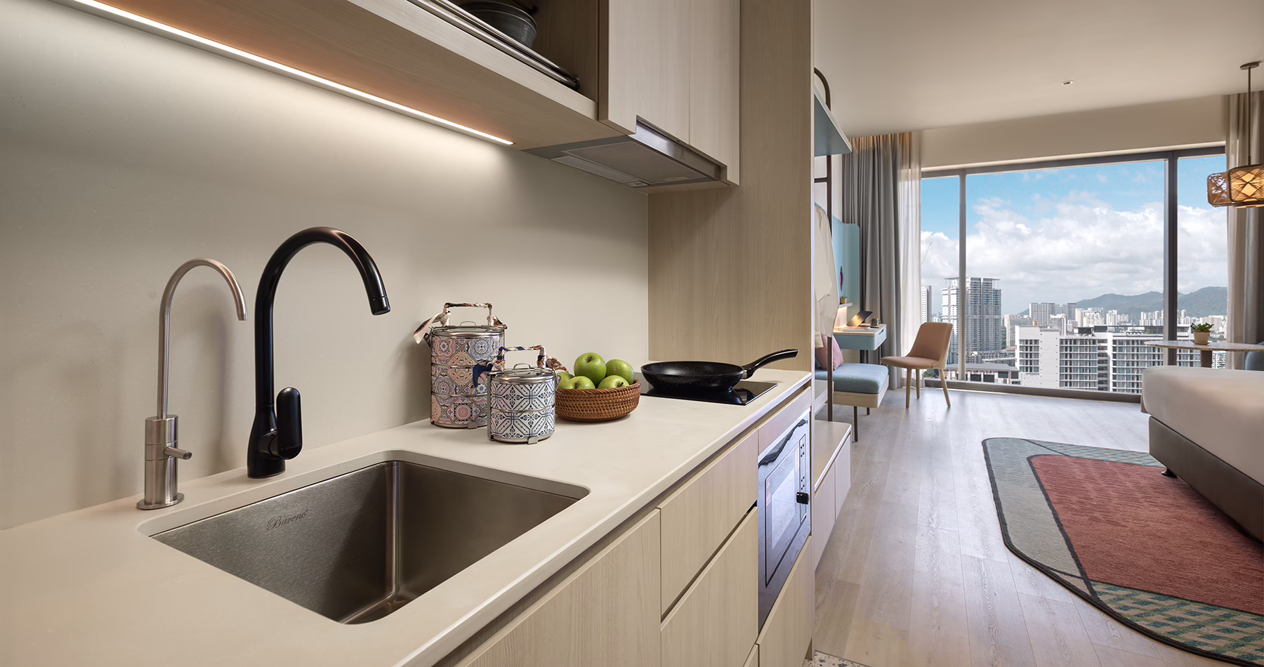 Kitchenette in a Premier King room at Capri by Fraser, Penang, featuring a sink, induction hob, modern cabinetry and an adjoining bedroom with city views.