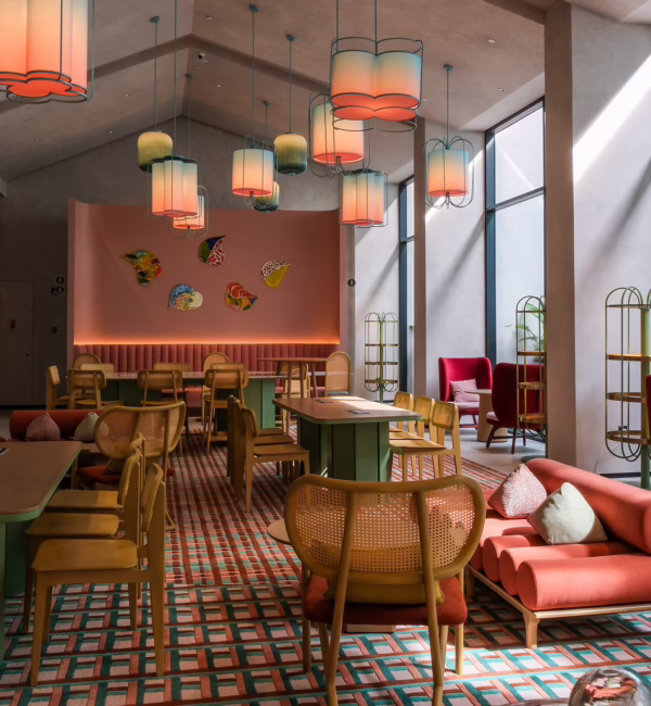 The Den at Capri by Fraser, Penang, featuring colourful lounge seating, communal tables, decorative lighting and floor-to-ceiling windows.