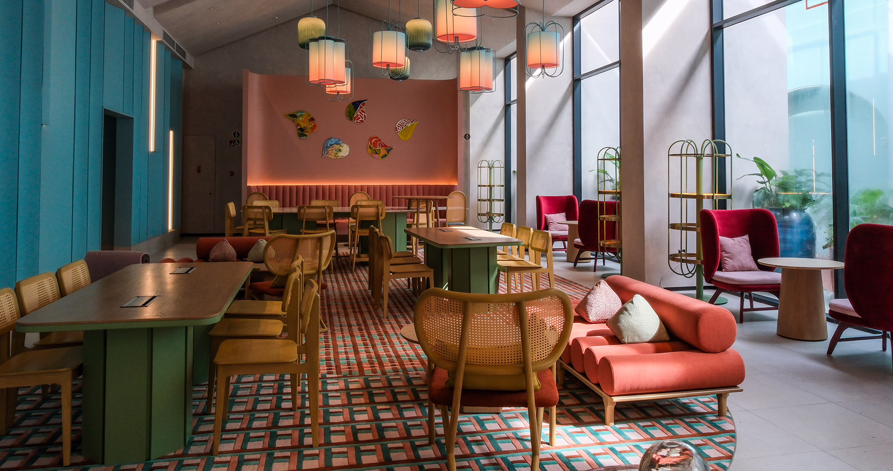 The Den at Capri by Fraser, Penang, featuring colourful lounge seating, communal tables, decorative lighting and floor-to-ceiling windows.