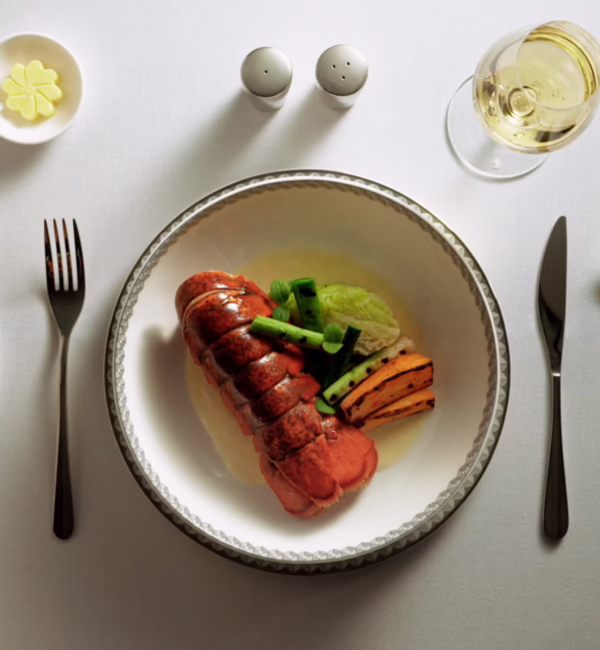 Poached Maine Lobster with Champagne Sauce (Suites and First Class Main Course) features slow-poached Maine lobster shell-on with buttery Savoy cabbage, grilled baby leeks, roasted sweet potatoes, borage cress, and a Champagne cream sauce