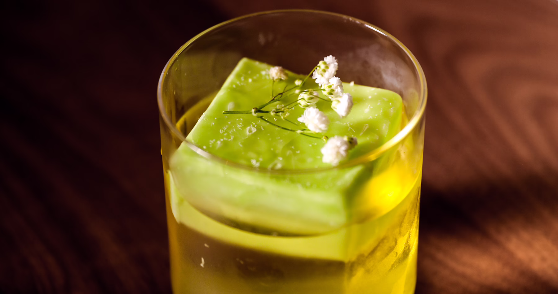 Green cocktail served over a large ice cube and finished with delicate floral garnish at Alma Luna Shanghai.