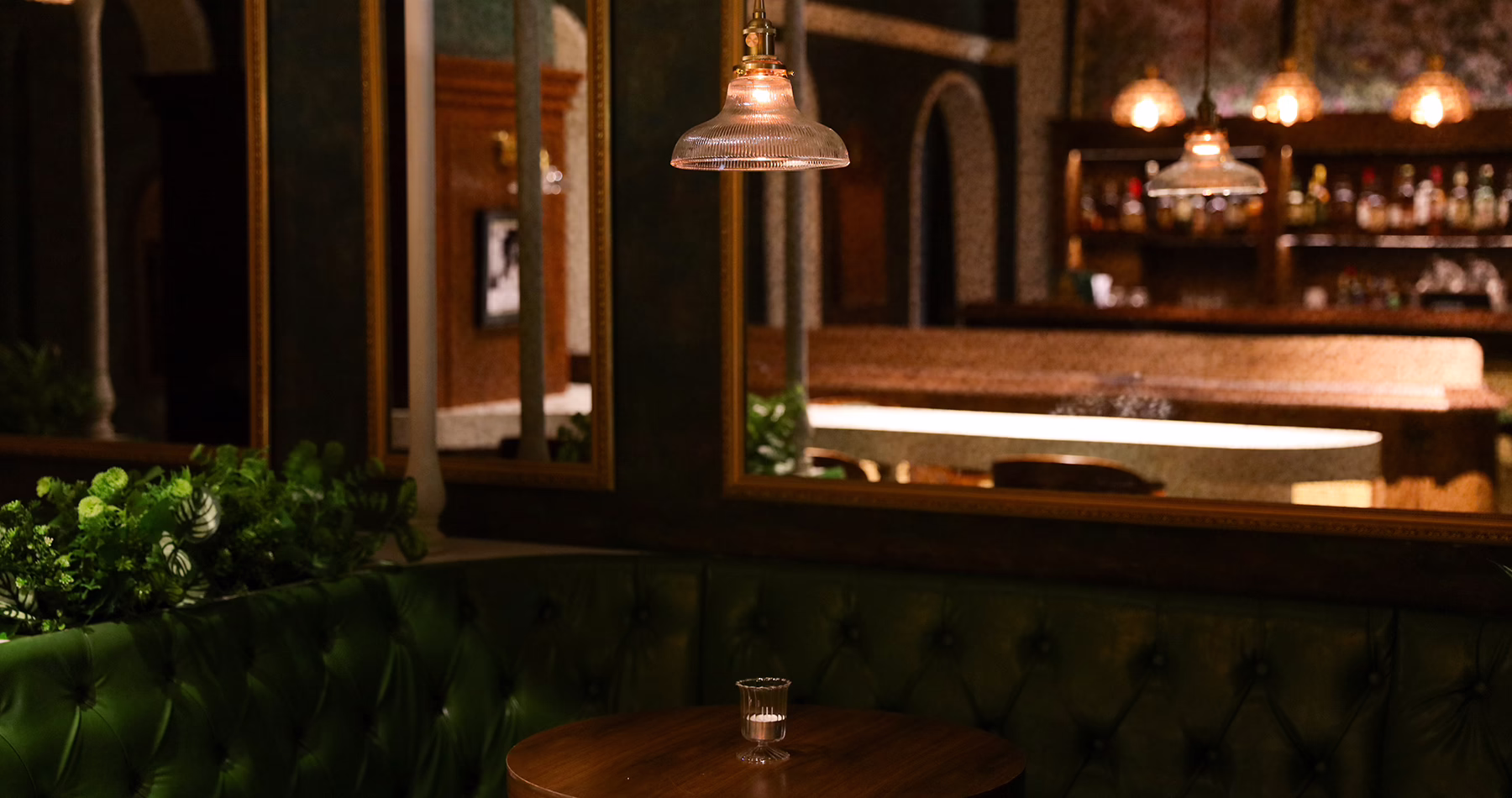 Intimate interior of Alma Luna Shanghai, featuring emerald-green leather seating, warm wood and vintage-style lighting.