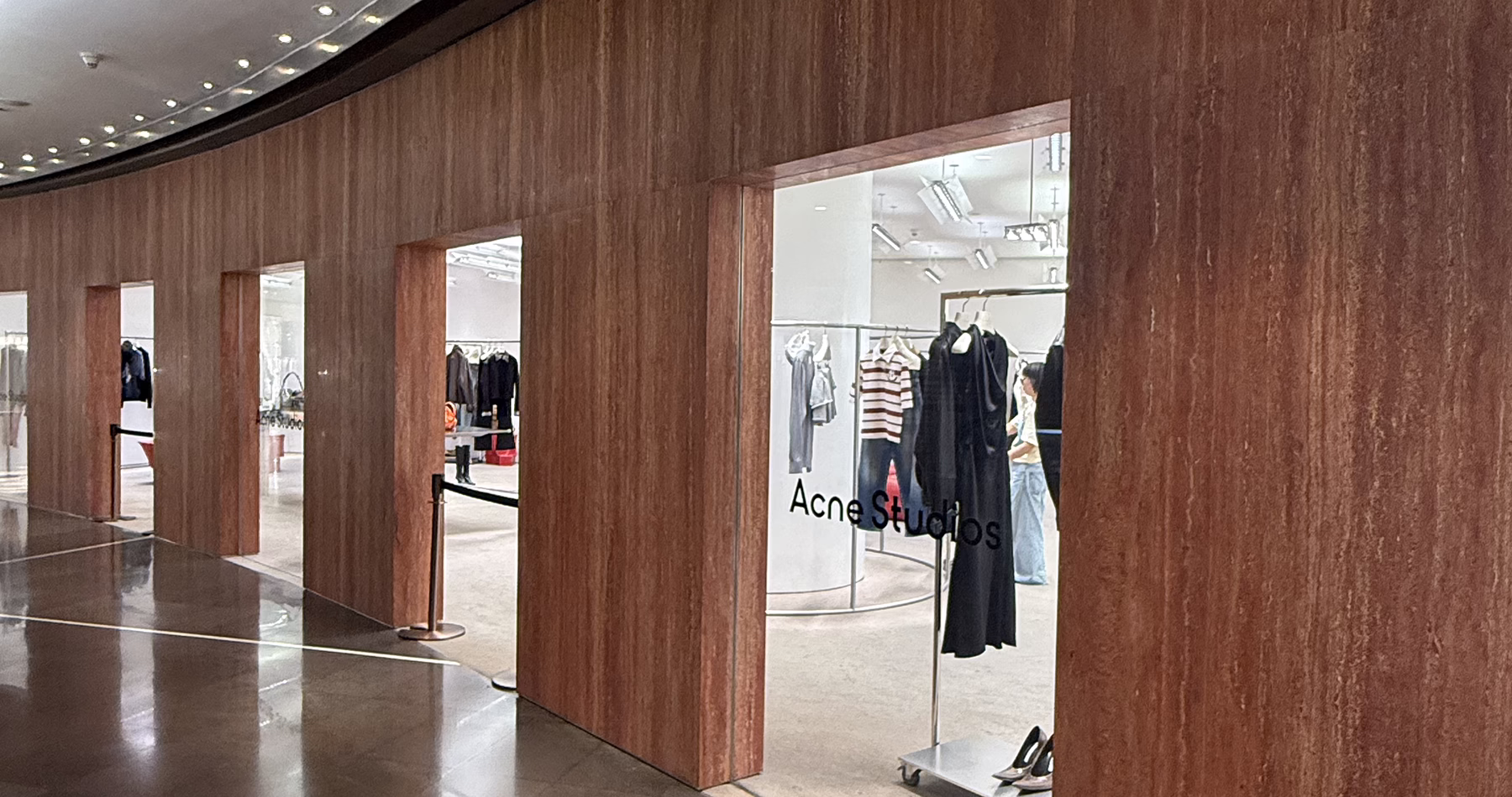 Acne Studios boutique at Reel Shanghai, featuring clothing displays framed by a curved wooden wall and minimalist interiors.