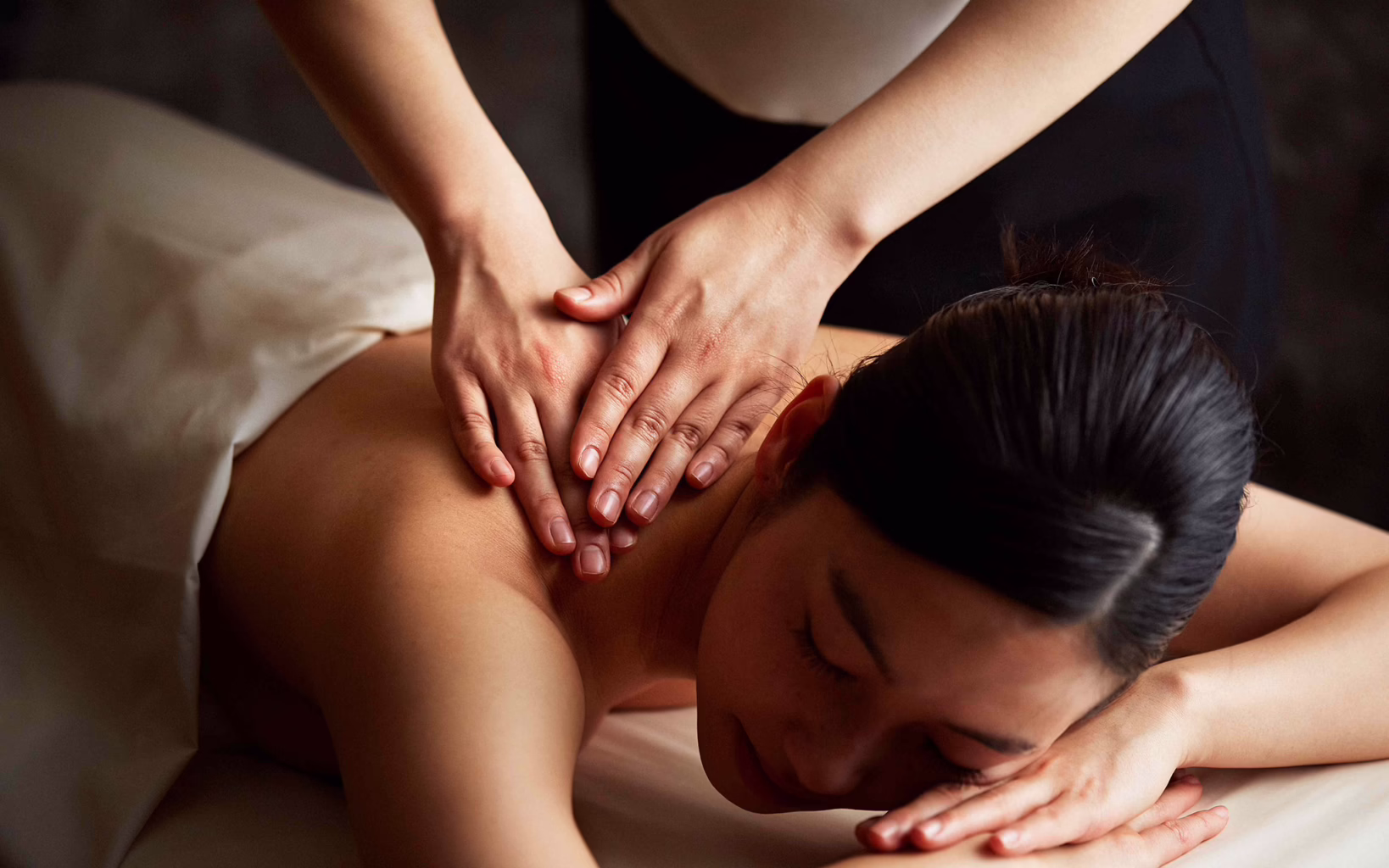 A woman lying face down on a massage bed as a therapist applies pressure to her upper back and shoulders at The Ritz-Carlton Spa, Singapore.