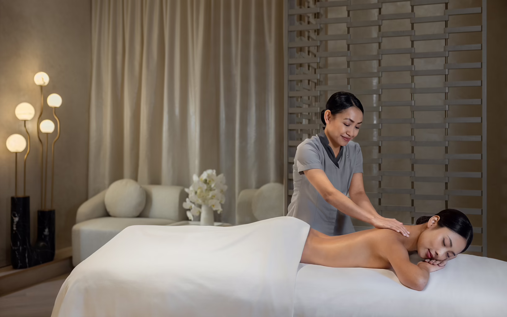 A therapist massages a guest's upper back at St. Regis Spa, The St. Regis Singapore, in an elegant treatment room with soft lighting and neutral interiors.