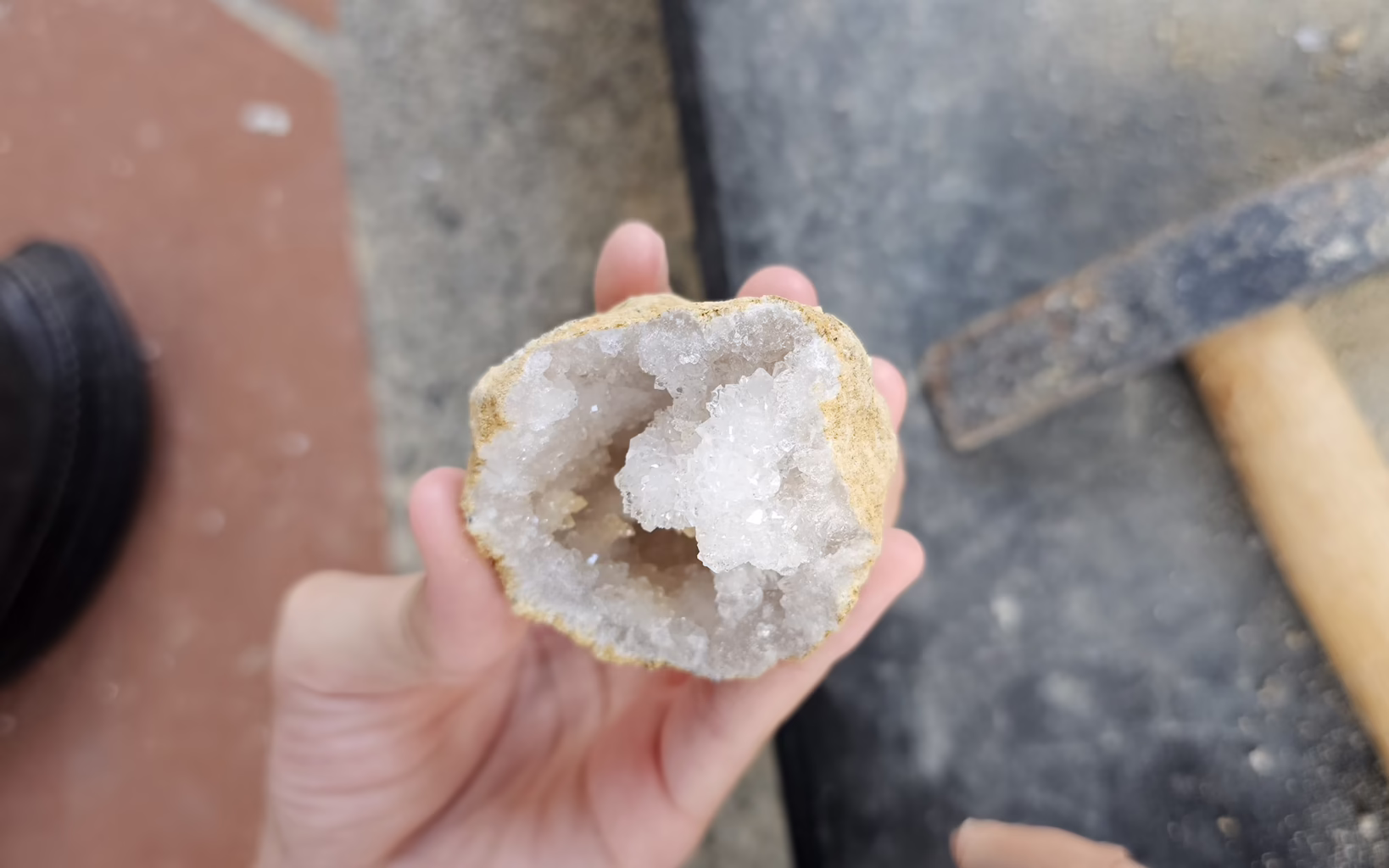 Close-up of an open geode held in a person's hand, revealing a hollow interior lined with sparkling white crystals at The Gem Museum in Singapore.