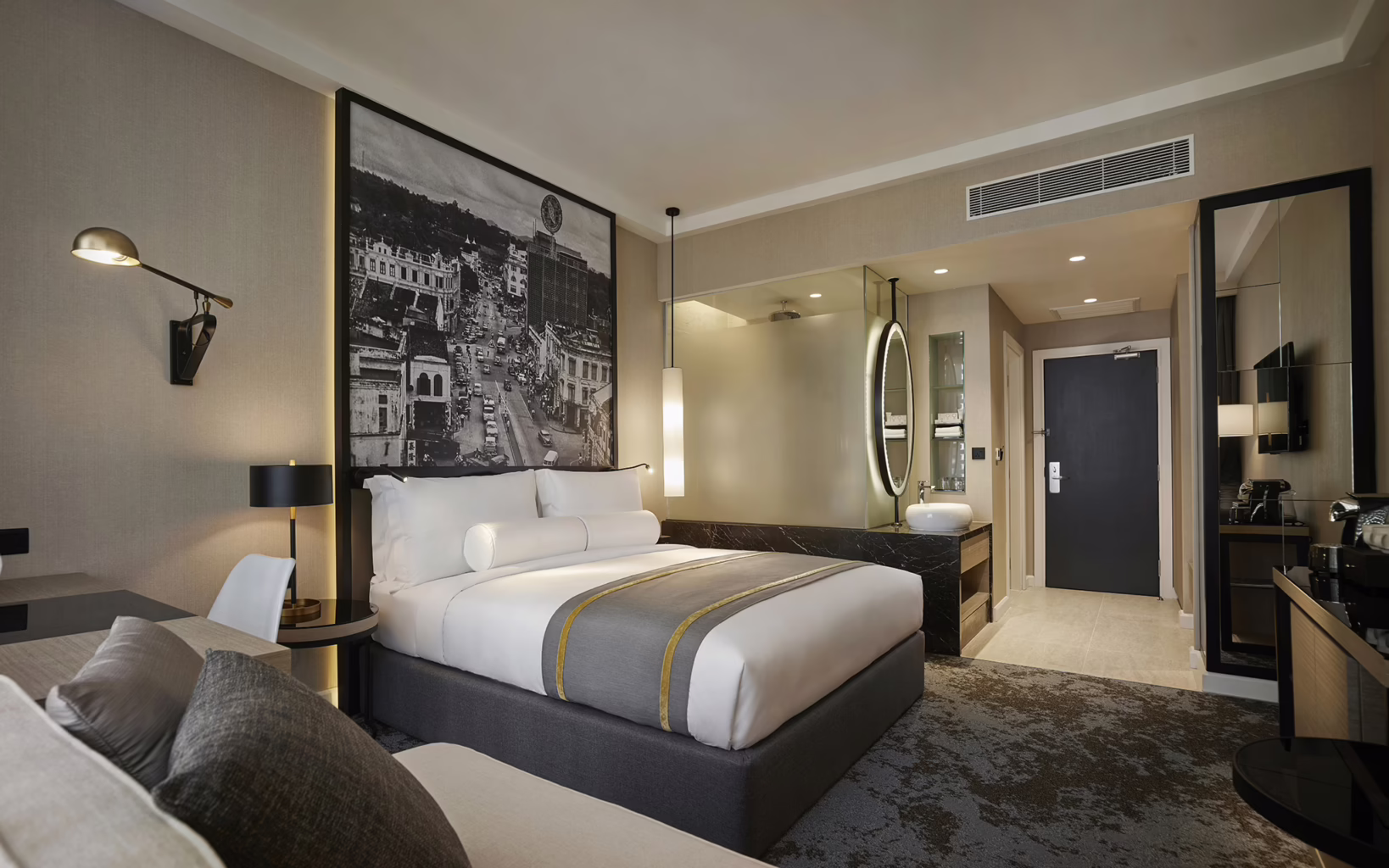 Deluxe King room at Hotel Stripes Kuala Lumpur, featuring a king-sized bed, contemporary furnishings, a black-and-white photograph of historic Kuala Lumpur and an open-plan vanity area.