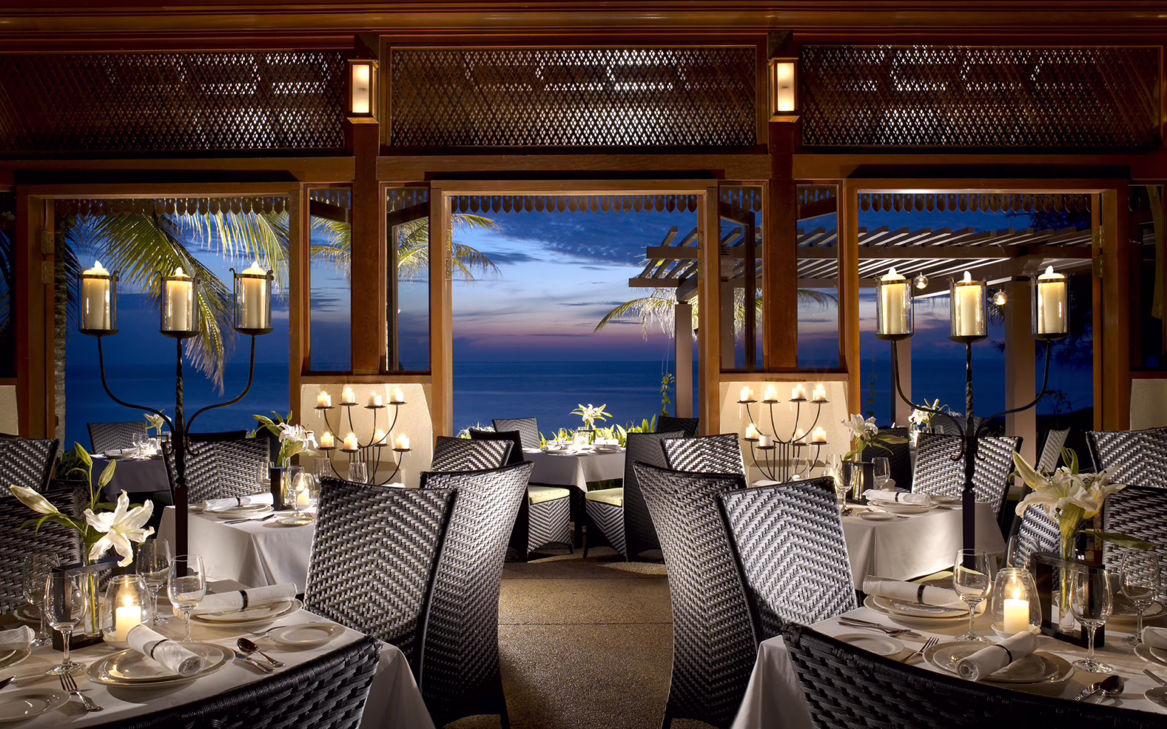 Nelayan restaurant at Tanjong Jara Resort, featuring candlelit tables, woven rattan chairs and traditional Malay-inspired timber interiors overlooking the South China Sea at dusk.