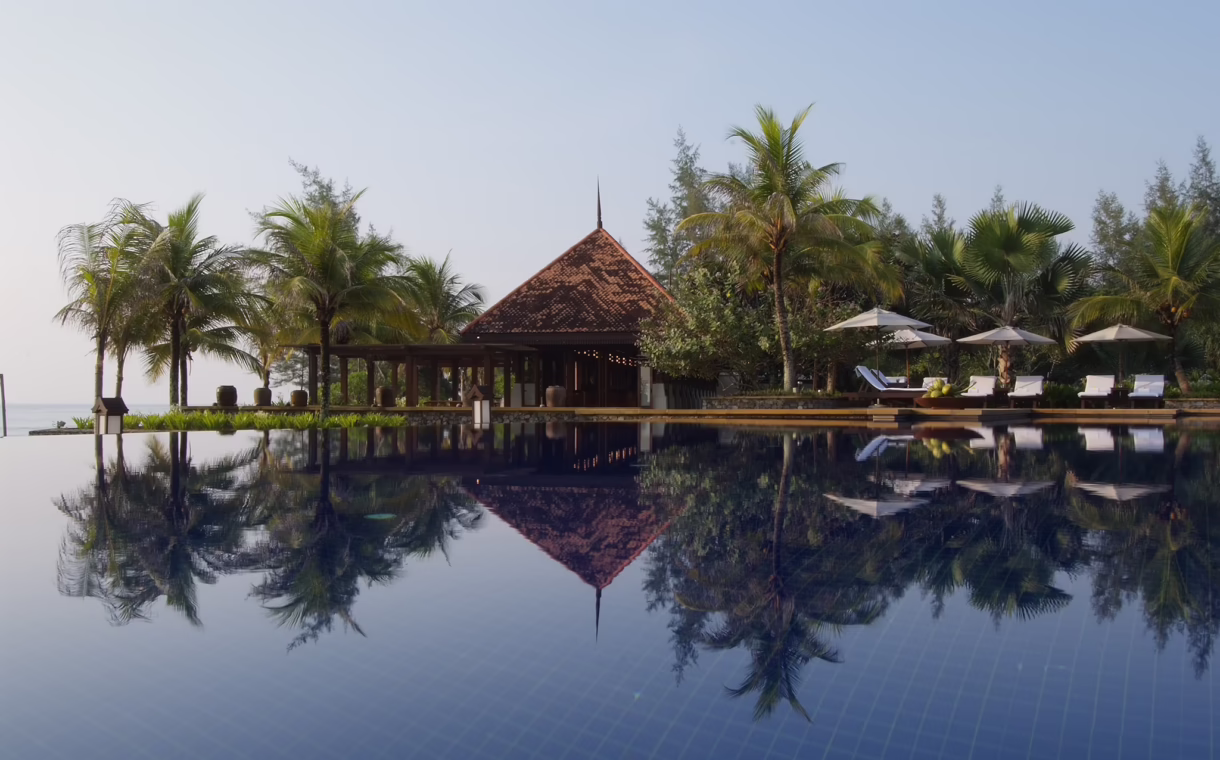 Infinity pool at Tanjong Jara Resort in Terengganu, reflecting a traditional Malay-style pavilion and surrounding palm trees, with sun loungers and umbrellas overlooking the South China Sea.