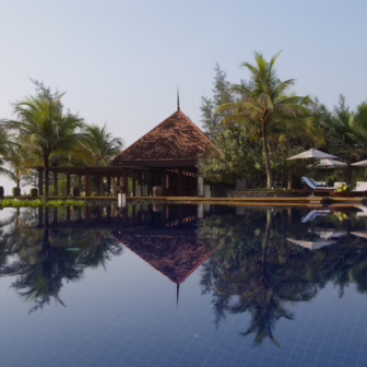 Infinity pool at Tanjong Jara Resort in Terengganu, reflecting a traditional Malay-style pavilion and surrounding palm trees, with sun loungers and umbrellas overlooking the South China Sea.